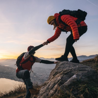 Hiker helping another person to summit a mountain